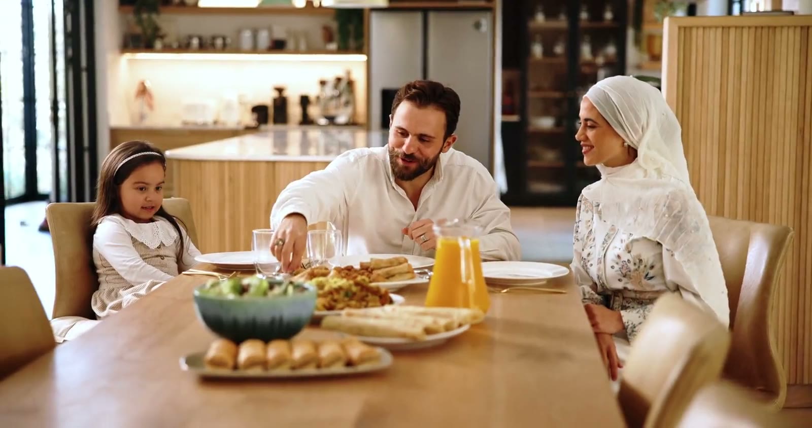 A father, a mother in hijab and their daughter sharing a meal at home