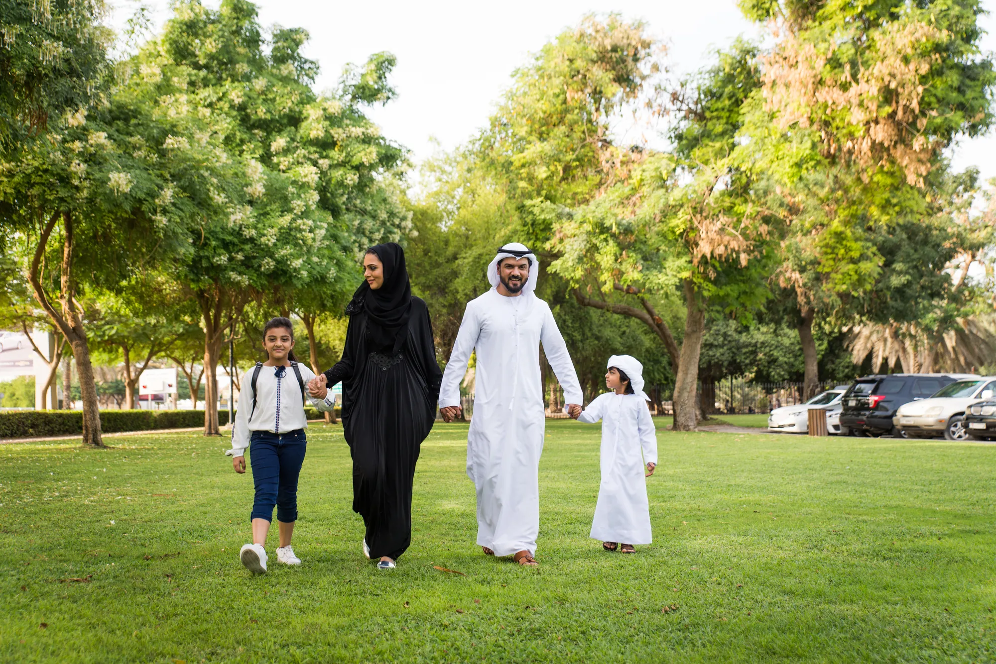 Parents and two children holding hands while walking through a leafy park